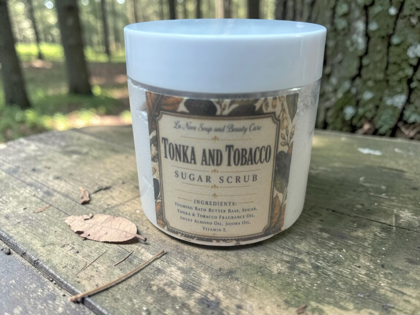 La Neve Soap and Beauty Care Tonka and Tobacco foaming sugar scrub in a clear jar on a rustic wooden surface.