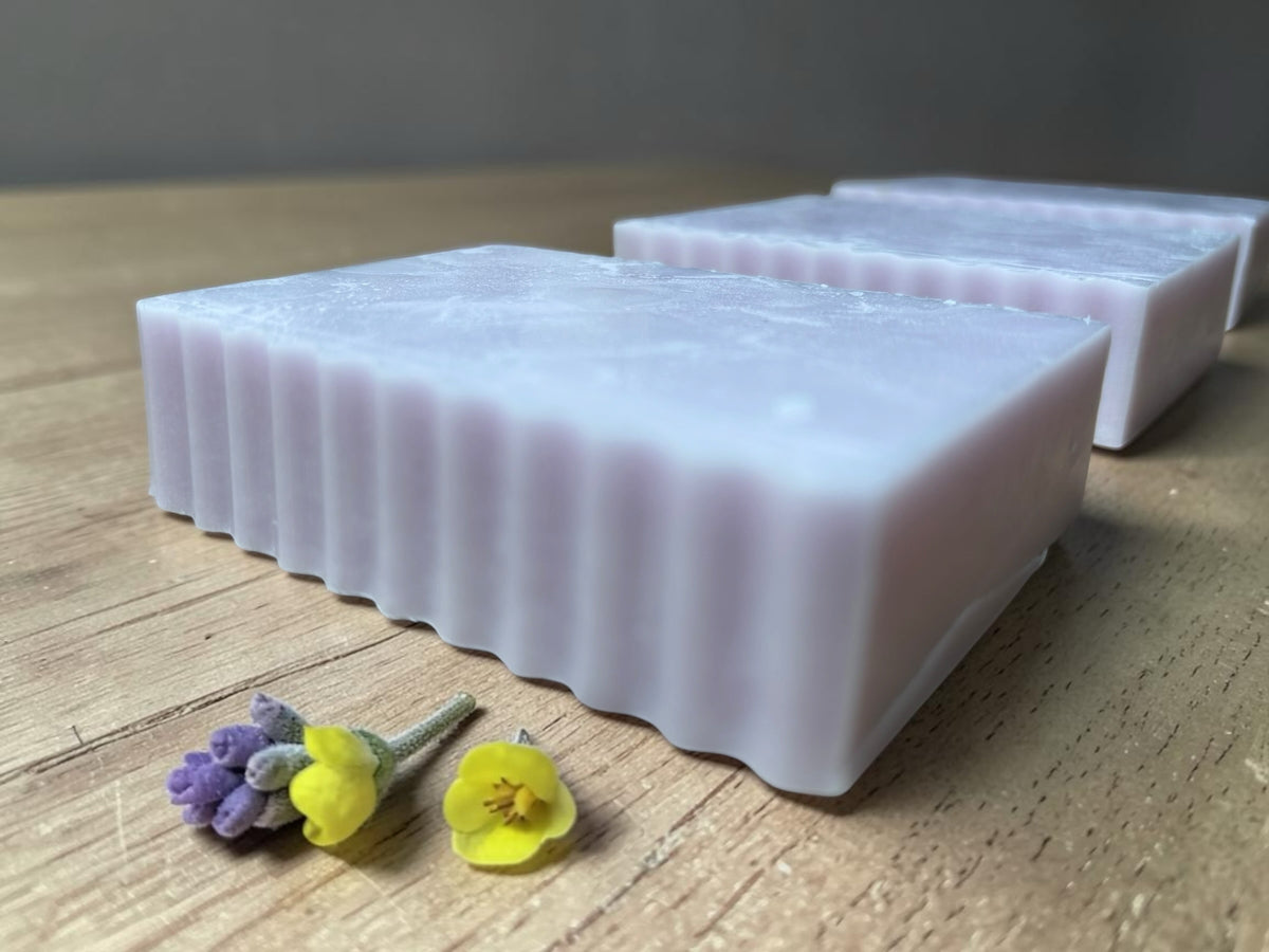 La Neve Soap and Beauty Care lavender botanical bar soap with a soft lilac hue and textured ridged edges on wood.