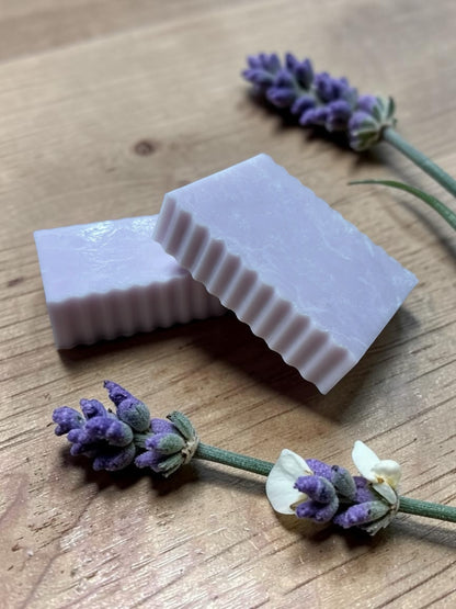 La Neve Soap and Beauty Care lavender botanical bar soap with fluted edges on a wooden surface with fresh lavender sprigs
