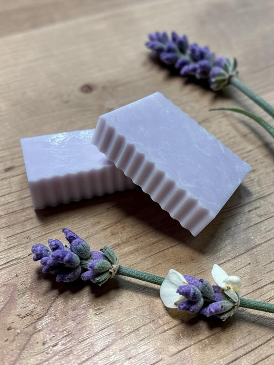 La Neve Soap and Beauty Care lavender botanical bar soap with fluted edges on a wooden surface with fresh lavender sprigs