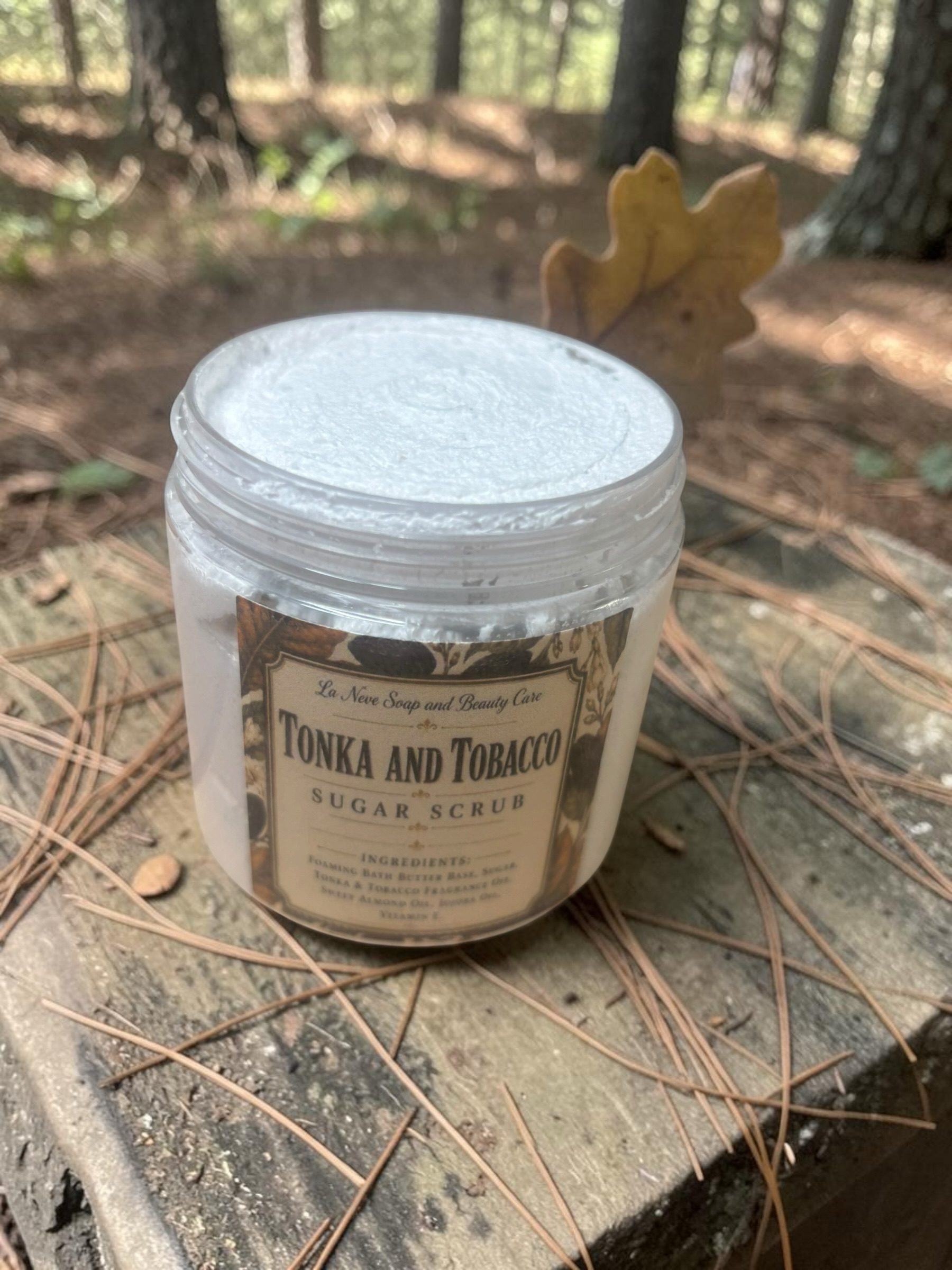 La Neve Soap and Beauty Care Tonka and Tobacco foaming sugar scrub in a clear jar on a rustic wooden surface.
