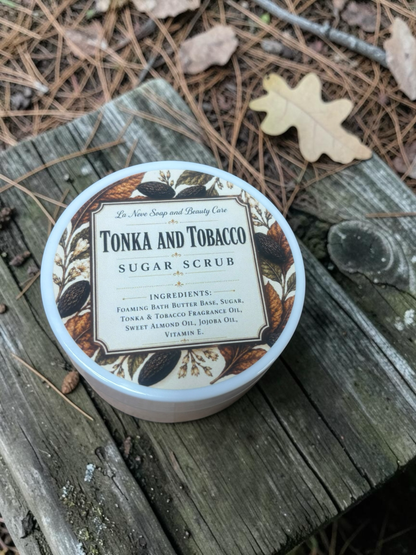La Neve Soap and Beauty Care Tonka and Tobacco sugar scrub in a white jar, placed on a rustic wooden surface.